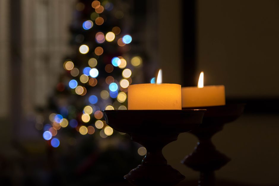 Warm candlelight with a Christmas tree in the background, creating a cozy holiday atmosphere.