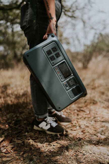 Person carrying a portable power station in rustic outdoor setting.