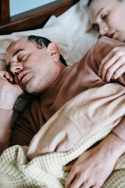 From above of crop adult female cuddling husband while sleeping together on comfortable bed