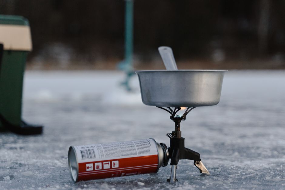 A camping stove setup on ice including a pot and butane canister for winter outdoor cooking.