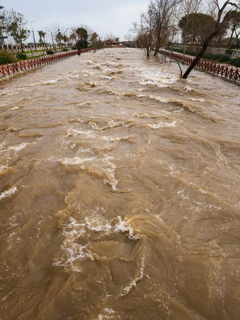 A turbulent river overflows its banks in a city during a seasonal rainstorm.